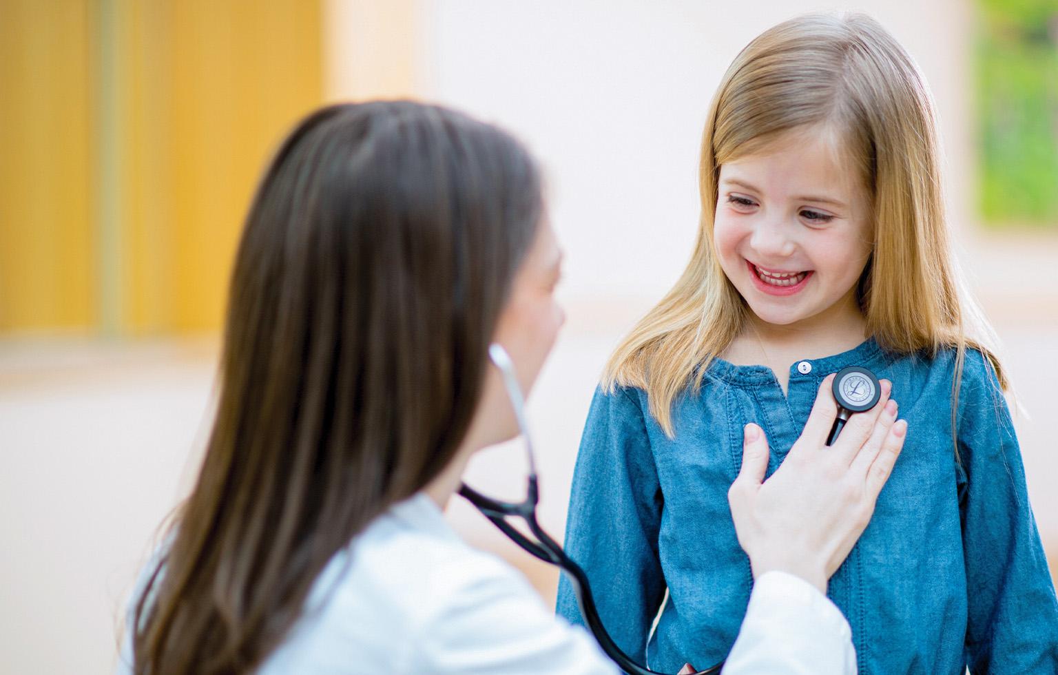 Emplify Health provider Kim Breidenbach listening to young girl's heartbeat with stethoscope. 