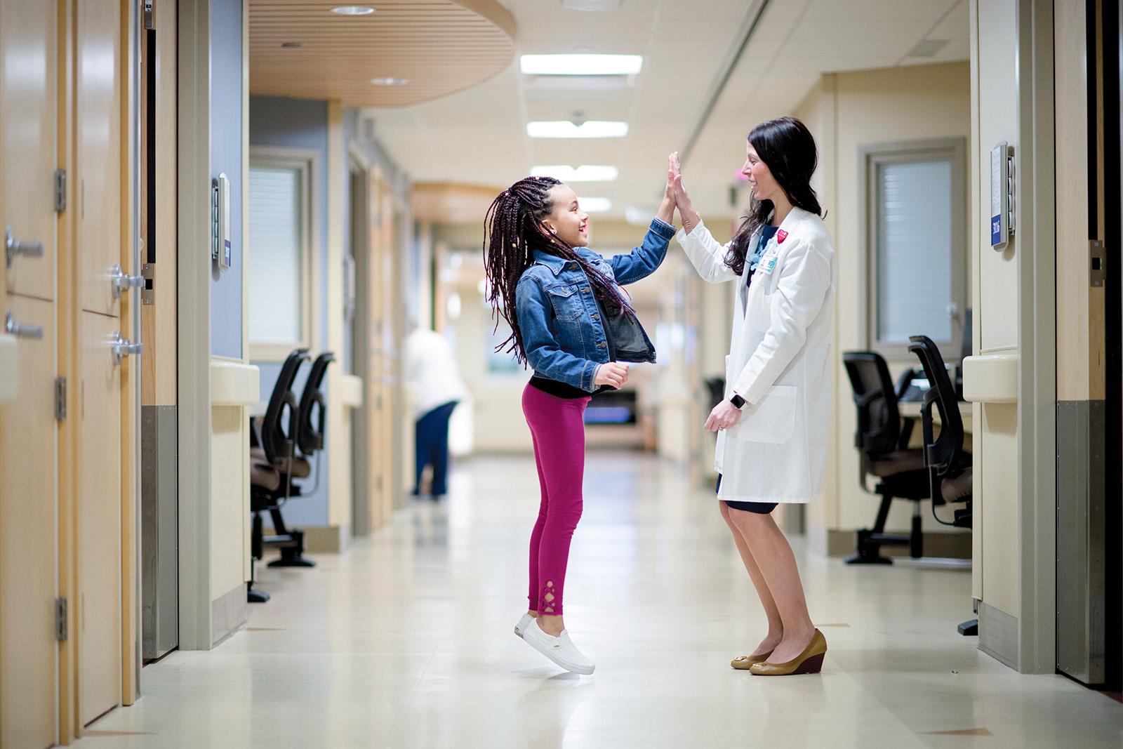 Emplify Health provider Stephanie Neuman, MD, high fiving young girl in clinic hallway.