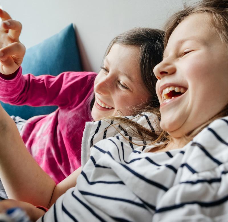 Two young girls laughing while playing on tablet.